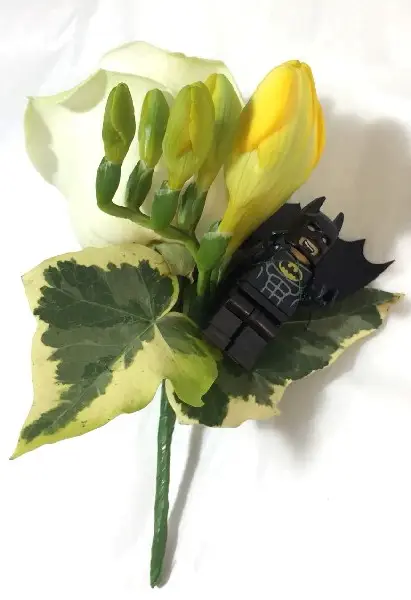 Groom buttonhole featuring white rose, yellow freesia and Batman LEGO man
