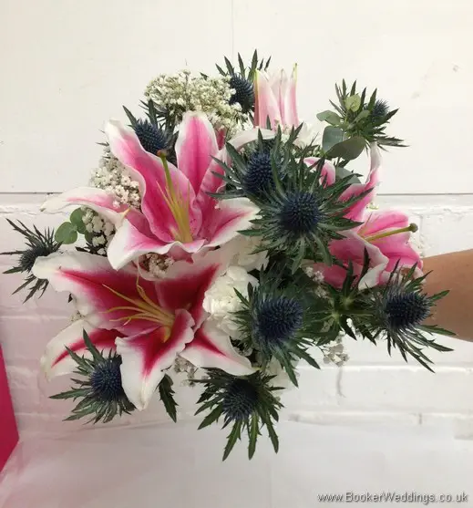 Bridal hand tied bouquet of Pink Stargazer lillies, white spray carnations, blue eryngium thistles, Gypsophila and Eucalyptus tilted view