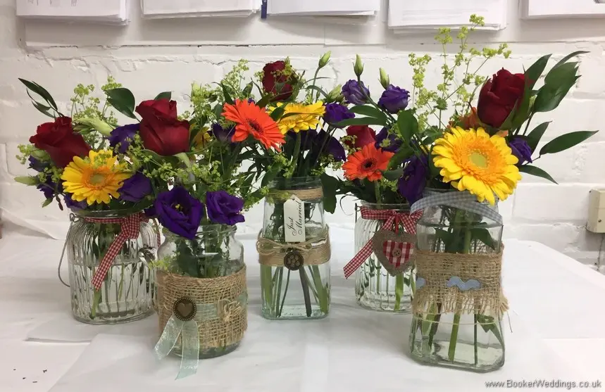 Bright and vibrant decorated jam jar just picked table centrepieces featuring roses, gerberas, lissianthus and alchamelia molis