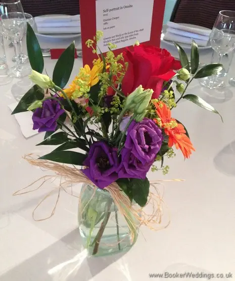Bright and vibrant jam jar table centrepieces featuring roses, gerberas, lissianthus and alchamelia molis at The Maritime Museum, Liverpool