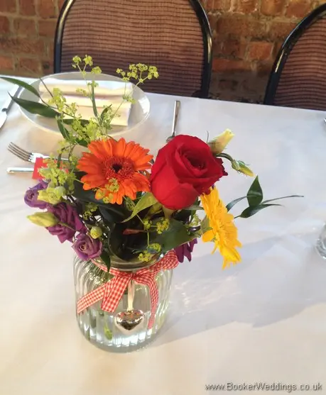 Bright and vibrant jam jar table decorations featuring roses, gerberas, lissianthus and alchamelia molis at the Maritime Museum, Liverpool