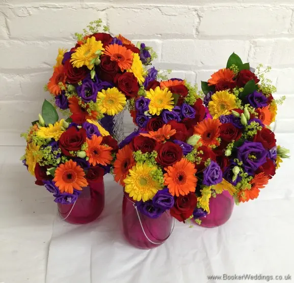 Bright and vibrant jam jar top table decorations featuring roses, gerberas, lissianthus and alchamelia molis side view