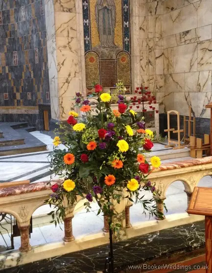Large pedestal arrangement featuring roses, gerberas, lissianthus and alchamelia molis at St Phillips Neri Church