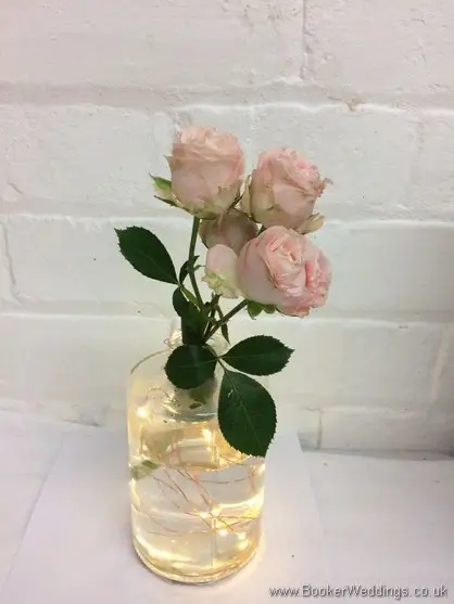 Pink roses in lit up bottle vase for table centrepieces