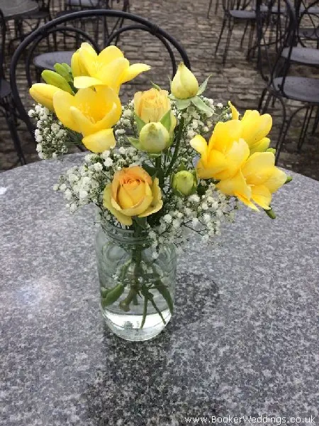 Wedding venue table centerpiece of yellow freesia and spray roses in jars