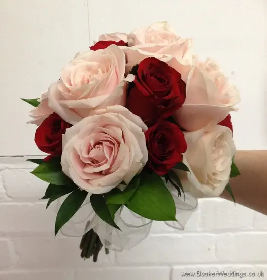 Bridal hand-tied bouquet featuring red and soft pink roses with a white organza bow tilted view