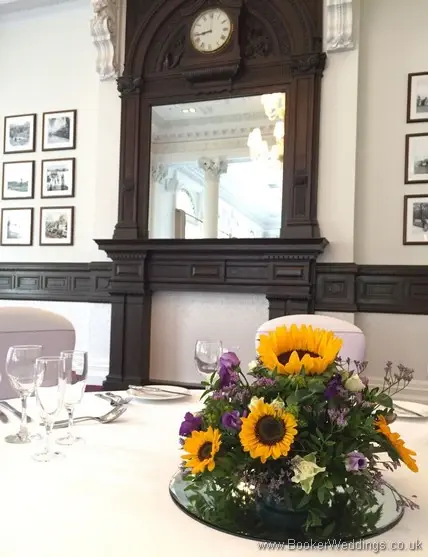 Low posy table centrepieces on mirror plate with sunflowers, yellow gerberas, white spray roses, purple lissianthus at Doubletree by Hilton Liverpool