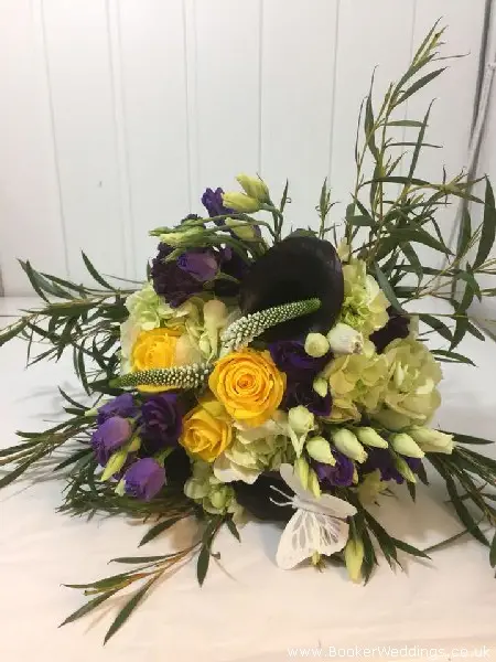 Bride hand-tied bouquet of just picked yellow and purple flowers including cala lily, roses, hydrangea, ranunculus, lissianthus, veronica